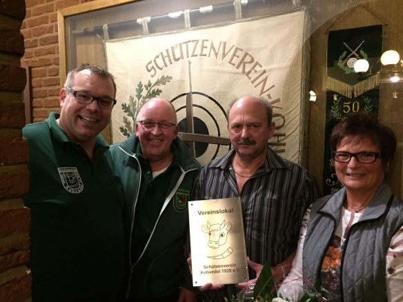 Vor dem Fahnenschrank un mit dem Schild "Vereinslokal" Oberst Björn, Vorsitzender Volker, Hansi und Elke Mölleck